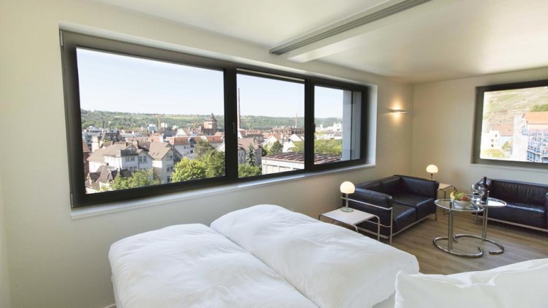 Modernes Apartment mit großem Fenster, Blick auf die Stadt, Doppelbett, schwarzem Sofa und kleinem Tisch mit Lampe., © Büroma-Apart Apartmentvermietung GmbH Modernes Apartment mit großem Fenster, Blick auf die Stadt, Doppelbett, schwarzem Sofa und kleinem Tisch mit Lampe., © Büroma-Apart Apartmentvermietung GmbH