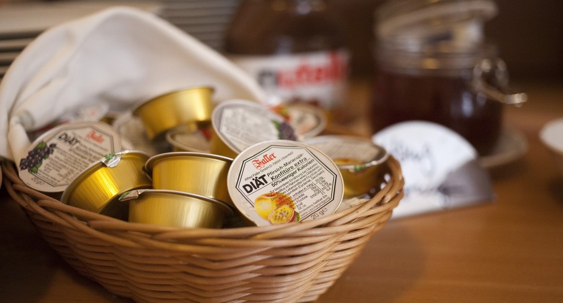 Ein Korb mit kleinen Marmeladenportionen steht auf einem Tisch. Im Hintergrund sind weitere Frühstückszutaten zu sehen., © AKZENT Hotel Torgauer Hof