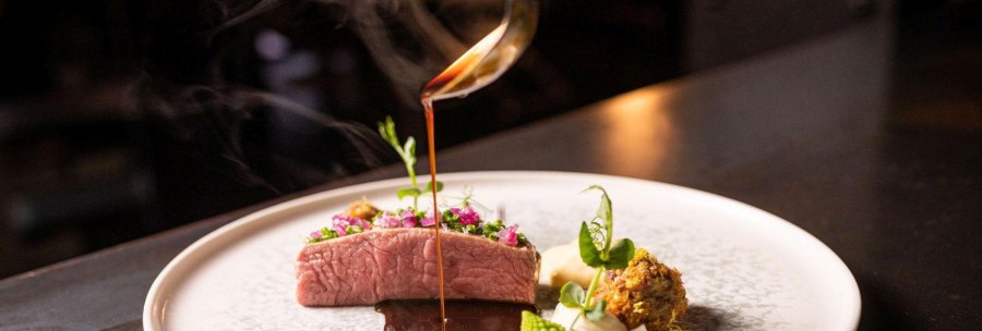 An artfully prepared gourmet dish with meat, vegetables and a dark sauce that is poured onto the plate from a ladle., &copy; 5 - Stuttgart