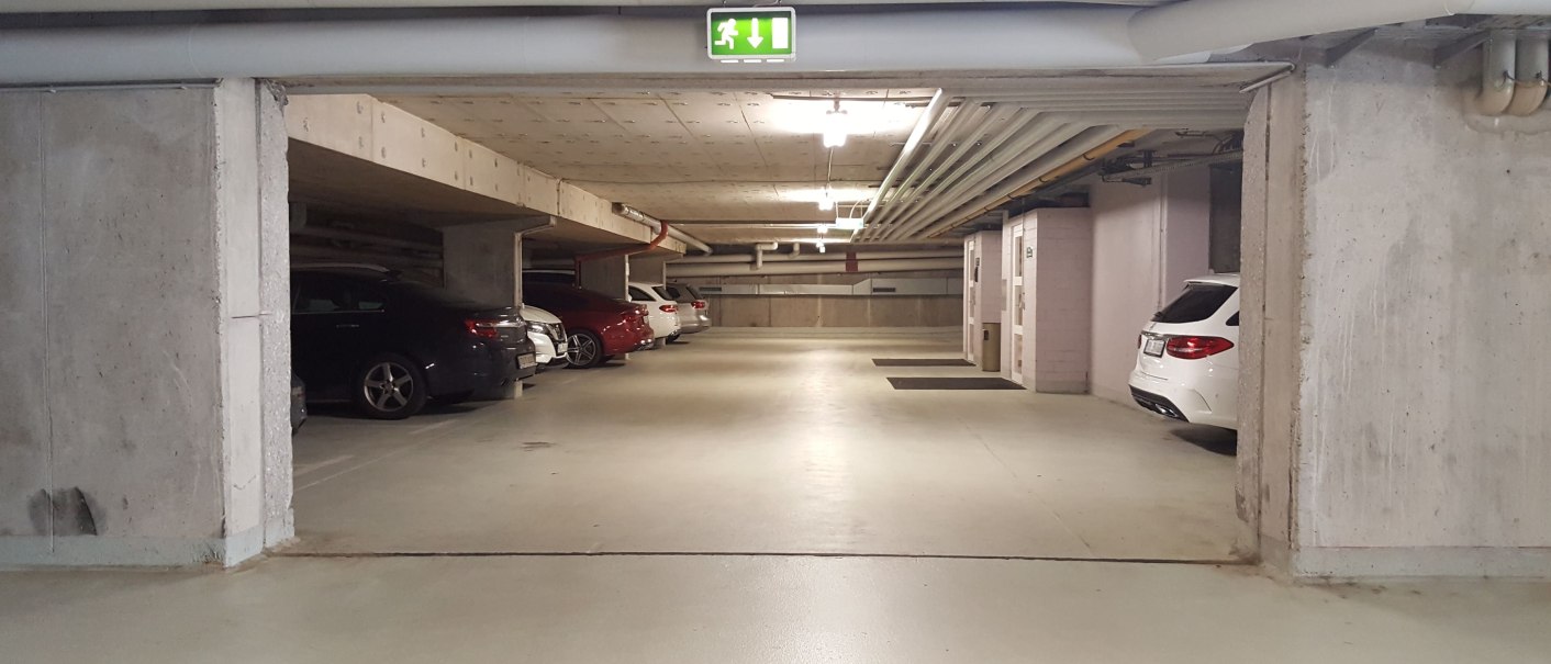 Underground parking lot with parked cars and an emergency exit sign on the ceiling., © Erikson Hotel