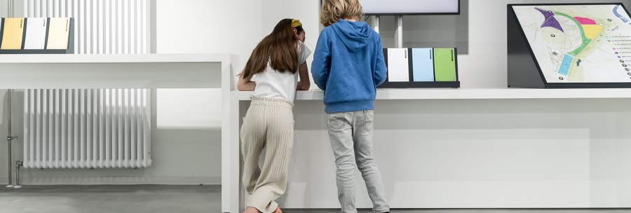 Zwei Kinder betrachten eine Ausstellungstafel in einem modernen Raum mit weißen Wänden und einem Heizkörper., © Stadt Stuttgart / Dominique Brewing