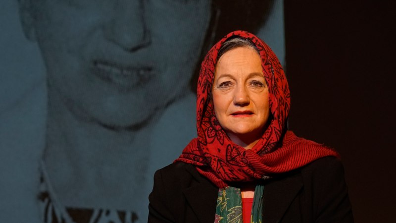 Eine Frau mit rotem Kopftuch steht vor einem großen Schwarz-Weiß-Foto einer anderen Frau. Sie trägt einen schwarzen Blazer und schaut direkt in die Kamera., © ©Katja Ritter Eine Frau mit rotem Kopftuch steht vor einem großen Schwarz-Weiß-Foto einer anderen Frau. Sie trägt einen schwarzen Blazer und schaut direkt in die Kamera., © ©Katja Ritter