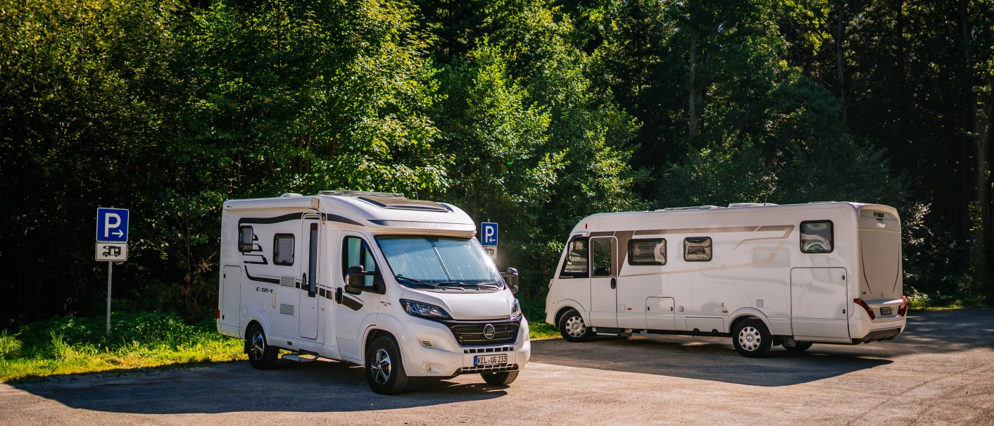 Zwei Wohnmobile parken auf einem Stellplatz am Waldrand. Die Sonne scheint, und es gibt Parkschilder im Hintergrund., &copy; Stuttgart-Marketing GmbH, Thomas Niederm&uuml;ller
