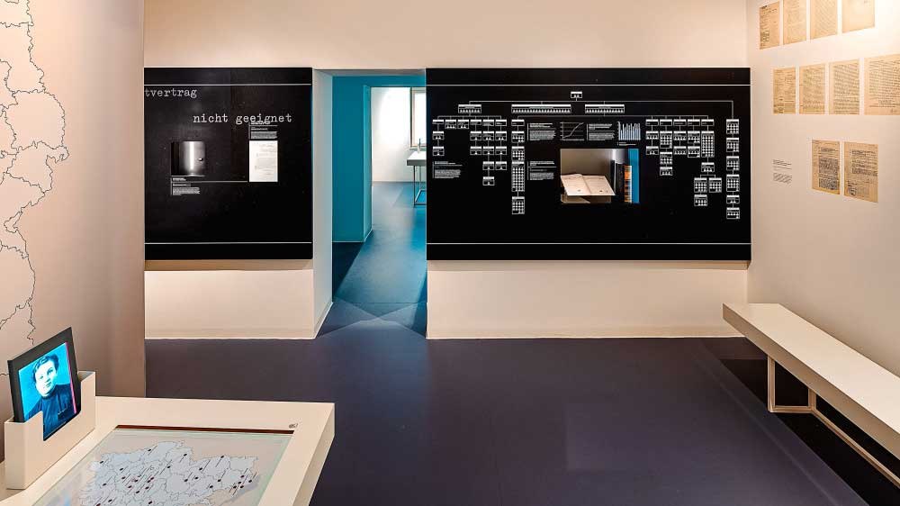 Ausstellungsraum im Hotel Silber mit Infotafeln, Dokumenten an der Wand und einem Bildschirm. Ein Tisch mit Karte und ein Durchgang sind sichtbar., © Haus der Geschichte Baden-Württemberg Ausstellungsraum im Hotel Silber mit Infotafeln, Dokumenten an der Wand und einem Bildschirm. Ein Tisch mit Karte und ein Durchgang sind sichtbar., © Haus der Geschichte Baden-Württemberg