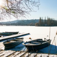 Verschneite Boote liegen an einem Steg am Max-Eyth-See. Die Sonne scheint durch die kahlen &Auml;ste, w&auml;hrend der See gefroren ist., &copy; Stuttgart-Marketing GmbH, Sarah Schmid