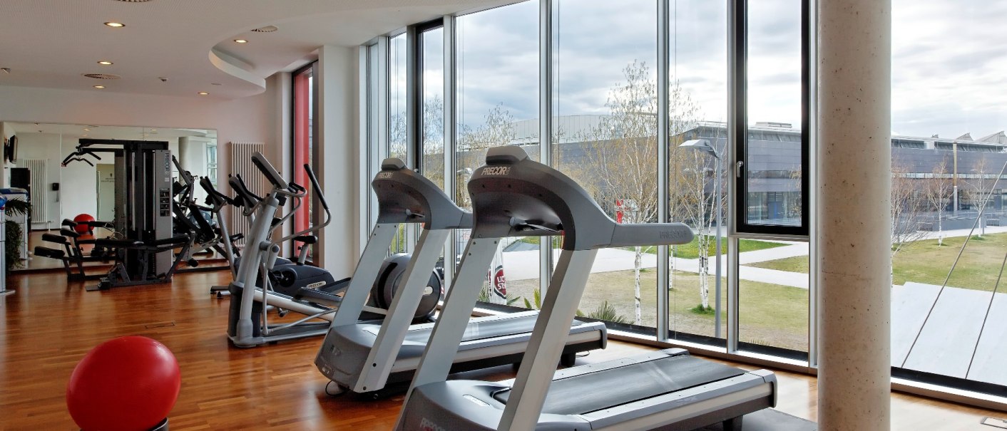 Moderner Fitnessraum im Hilton Garden Inn mit Laufbändern, Fitnessgeräten und großen Fenstern mit Blick nach draußen., © Hilton Garden Inn Stuttgart Neckarpark