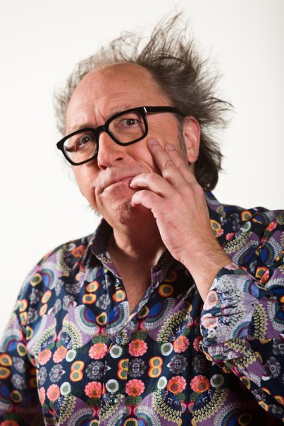 Ein Mann mit zerzaustem Haar und bunter Brille trägt ein auffälliges, gemustertes Hemd. Er berührt nachdenklich sein Gesicht., © Theaterhaus Stuttgart e.V.