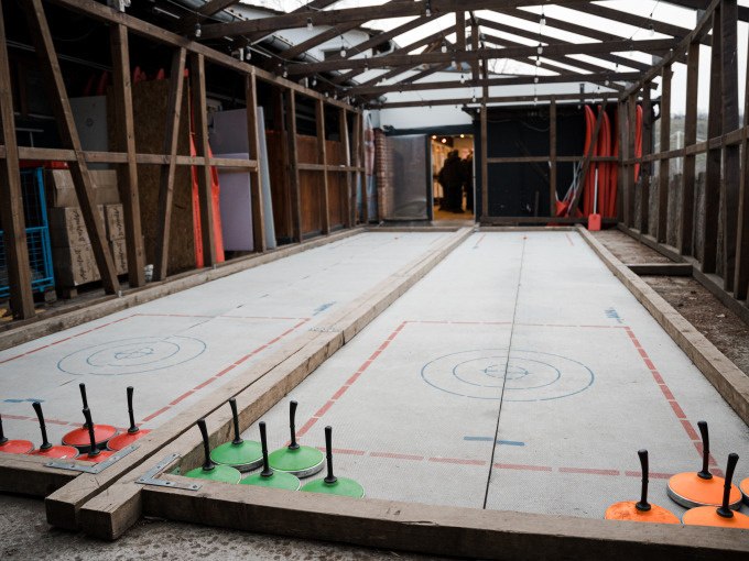 Covered curling rink with curling sticks in green and orange. The rink is made of concrete and surrounded by wooden beams., &copy; Cool-Tours StattReisen