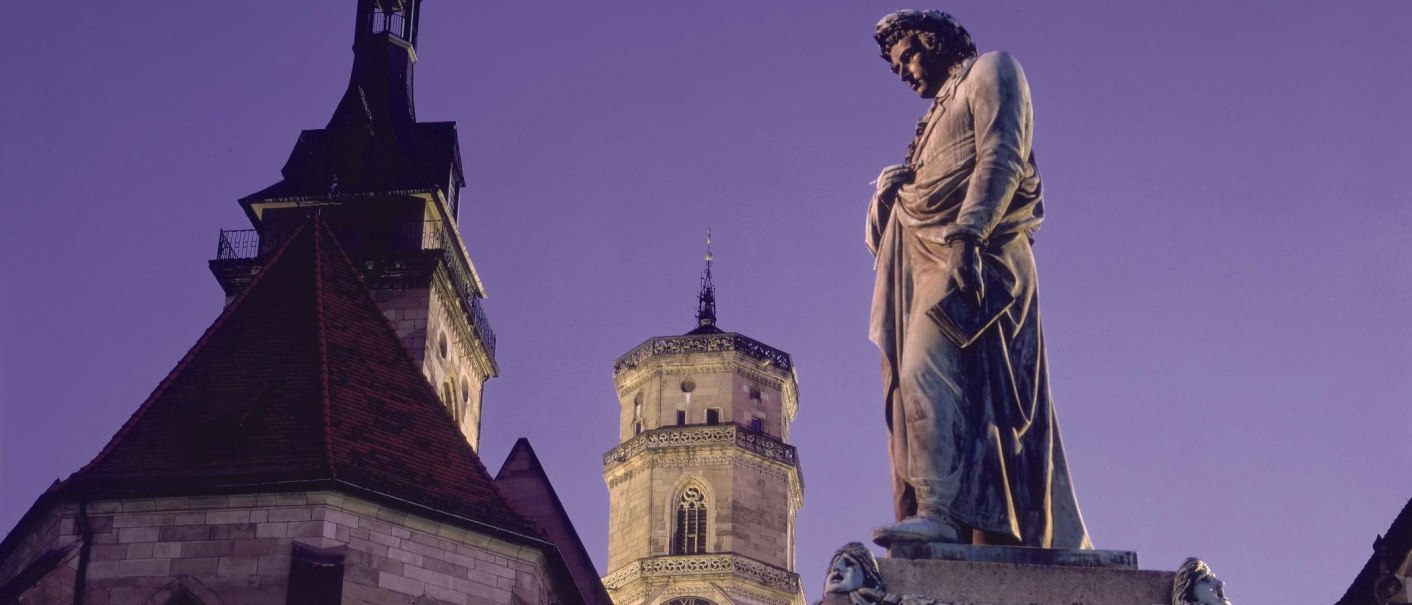 Die Stiftskirche und das Schillerdenkmal bei Dämmerung. Die Statue steht im Vordergrund, während die Kirche im Hintergrund zu sehen ist., © Stuttgart-Marketing GmbH Die Stiftskirche und das Schillerdenkmal bei Dämmerung. Die Statue steht im Vordergrund, während die Kirche im Hintergrund zu sehen ist., © Stuttgart-Marketing GmbH