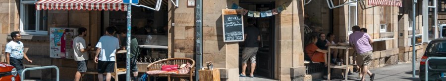 Caf&eacute;bar Auszeit on a street corner with a red awning. People are sitting outside, street signs and cars are visible., &copy; SMG, Sarah Schmid