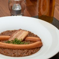Linseneintopf mit W&uuml;rstchen und Speck in einem wei&szlig;en Teller, daneben eine Sch&uuml;ssel Sp&auml;tzle auf einem Holztisch., &copy; Stuttgart-Marketing GmbH