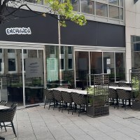 Outdoor area of a restaurant called Enchilada with empty tables and chairs. A tree and plants separate the seating areas., © SMG Outdoor area of a restaurant called Enchilada with empty tables and chairs. A tree and plants separate the seating areas., © SMG