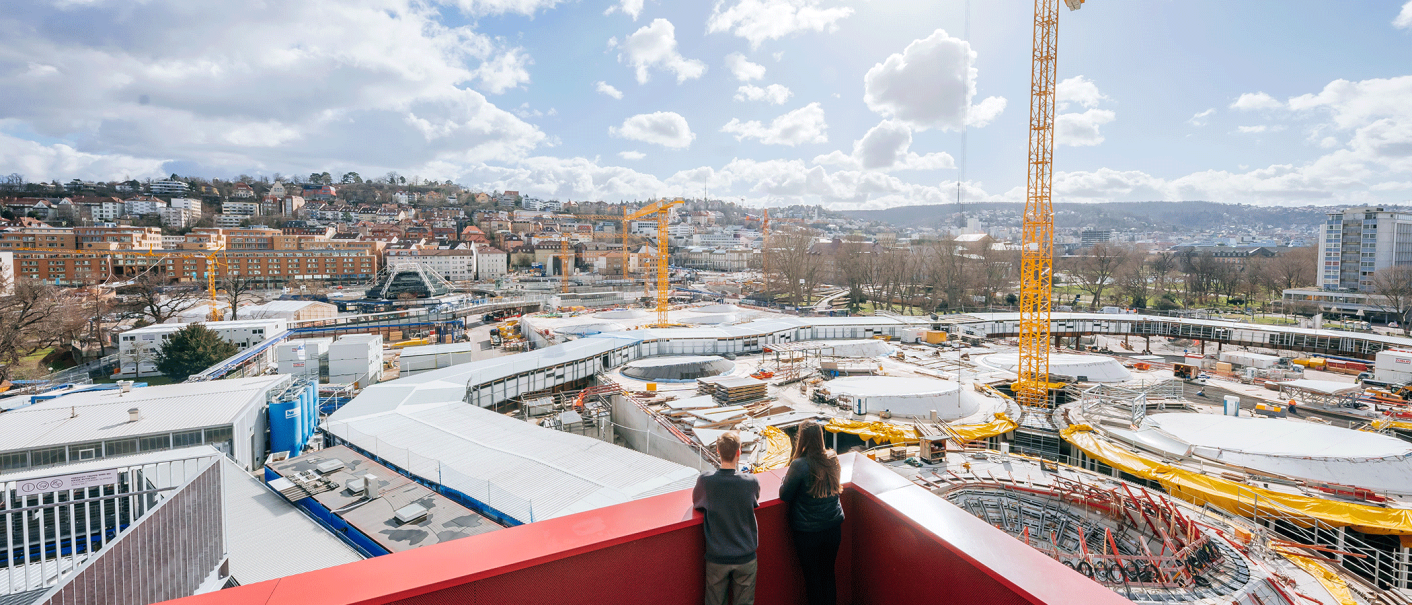 Two people stand on a roof terrace and look out over a large construction site with cranes and a city in the background., &copy; Thomas Niederm&uuml;ller