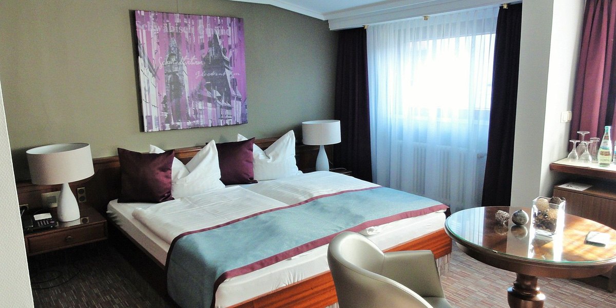 A comfortable double room with a large bed, two nightstands, a table, and chairs. Light-colored curtains and modern wall decor., &copy; Hotel Pelikan