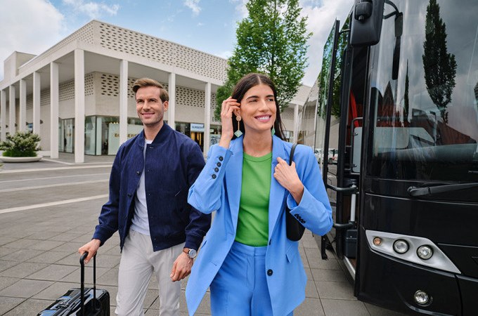 Two people get off a bus in front of a modern building. They look cheerful and are wearing fashionable clothes., © Schlienz-Tours GmbH & Co.KG Two people get off a bus in front of a modern building. They look cheerful and are wearing fashionable clothes., © Schlienz-Tours GmbH & Co.KG