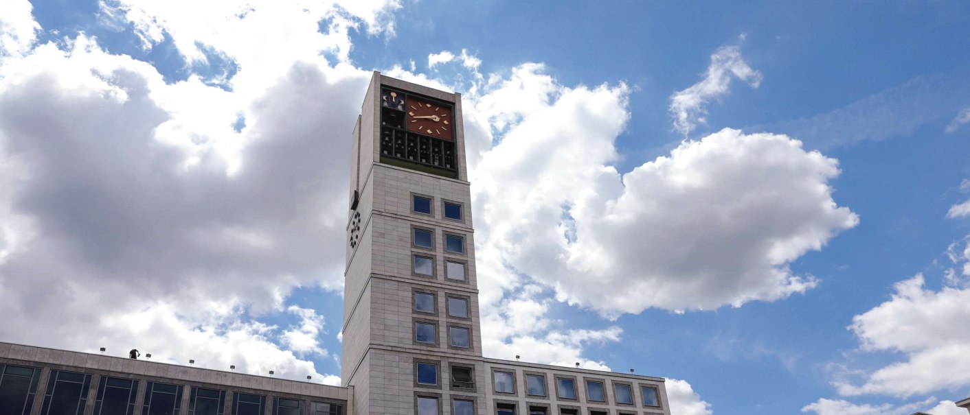 A modern building with a tall clock tower and lots of windows. The sky is blue with a few clouds., &copy; Fei Shiyu