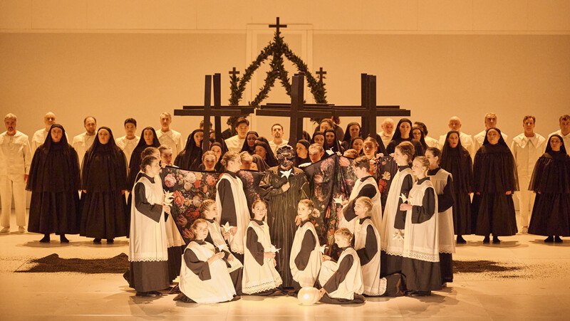 Opernszene aus "Otello" mit Chor in schwarz-weißer Kleidung vor großen Kreuzen. Die Bühne ist minimalistisch gestaltet., © Württembergische Staatstheater Stuttgart