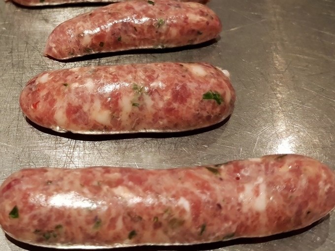 Raw sausages lie on a metal surface, ready for further processing. They are streaked with herbs., © Kultweine-Kochwelten-Kunstücke - Kochschule Sonja Lenz Raw sausages lie on a metal surface, ready for further processing. They are streaked with herbs., © Kultweine-Kochwelten-Kunstücke - Kochschule Sonja Lenz
