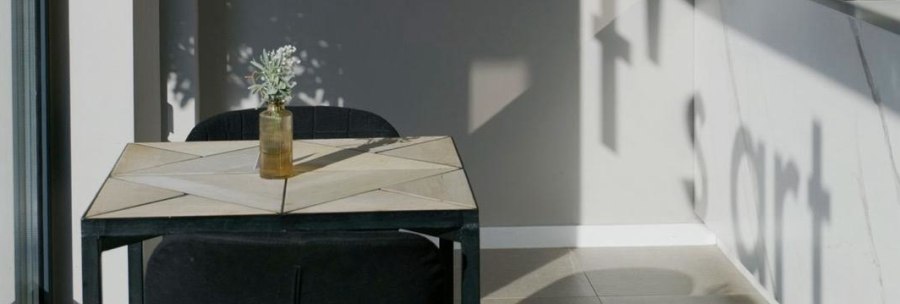 Heller Raum mit Tisch, zwei schwarzen St&uuml;hlen und einer kleinen Vase; an der Wand f&auml;llt der Schatten des Wortes &bdquo;Short&ldquo;., &copy; Taraba