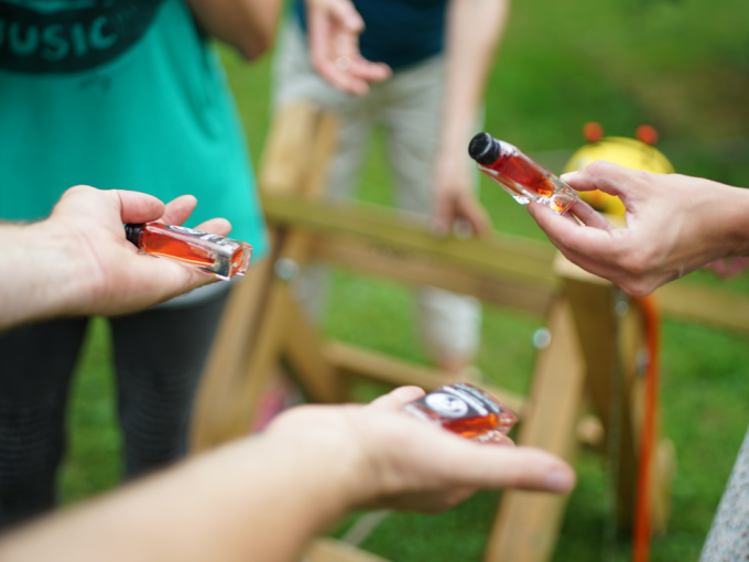 Mehrere Personen halten kleine Flaschen mit roter Fl&uuml;ssigkeit. Im Hintergrund ist ein Holzbock zu sehen., &copy; Cool-Tours StattReisen