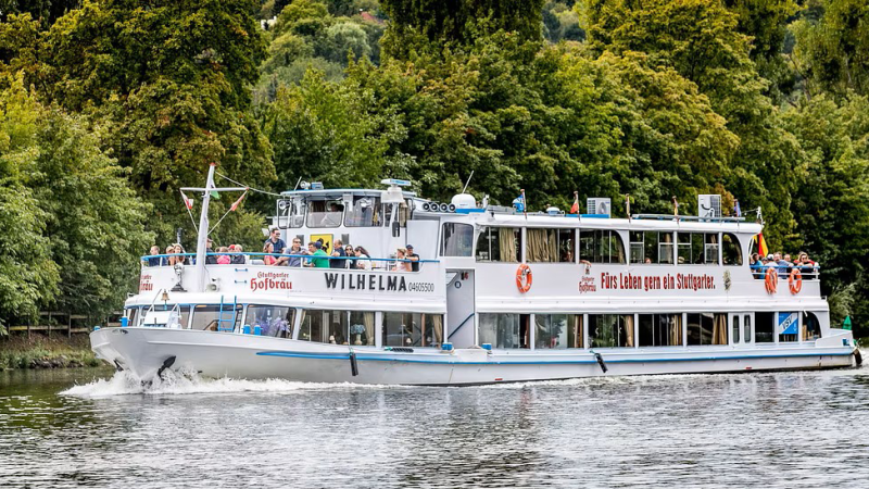 Das Ausflugsschiff fährt auf einem Fluss, umgeben von üppigem Grün. An Bord sind viele Passagiere, die die Aussicht genießen., © NeckarFlair MS Wilhelma Betriebsgesellschaft mbH Das Ausflugsschiff fährt auf einem Fluss, umgeben von üppigem Grün. An Bord sind viele Passagiere, die die Aussicht genießen., © NeckarFlair MS Wilhelma Betriebsgesellschaft mbH
