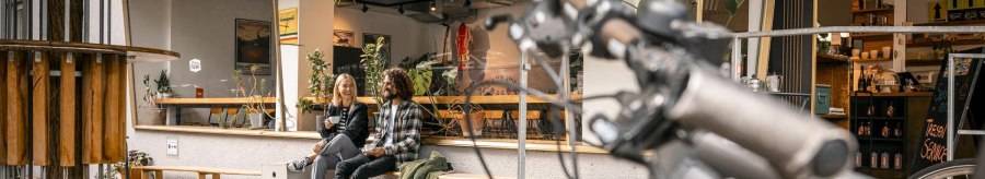 Two people are sitting on a bench in front of a caf&eacute;, laughing. A bicycle handlebar can be seen in the foreground. Autumn leaves lie on the ground., &copy; SMG Stuttgart Marketing GmbH - Sarah Schmid