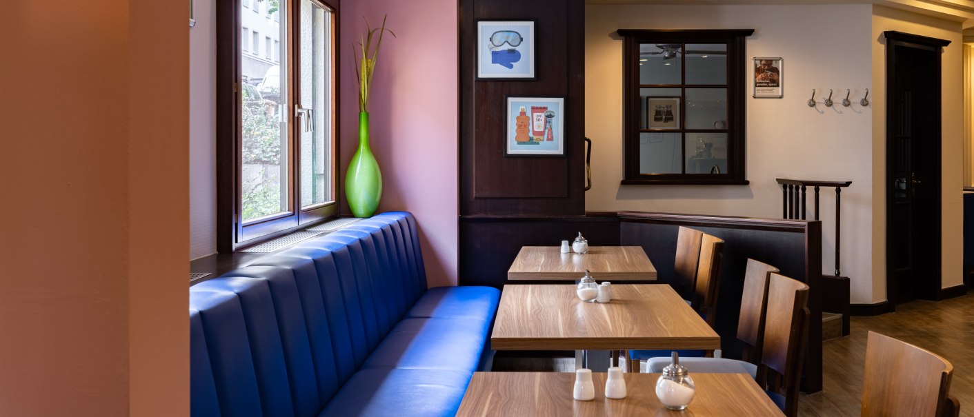 A cozy breakfast room with blue benches, wooden tables, and decorative pictures on the walls. Large windows let in natural light., &copy; Novum  Hospitality