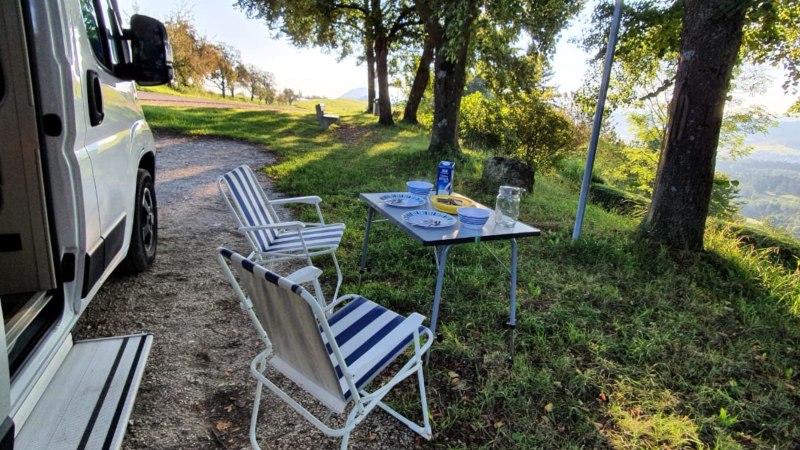 Wohnmobilstellplatz mit Tisch und Stühlen im Grünen. Teller und Gläser auf dem Tisch, umgeben von Bäumen und mit Blick auf die Landschaft., © Stadtmarketing Göppingen