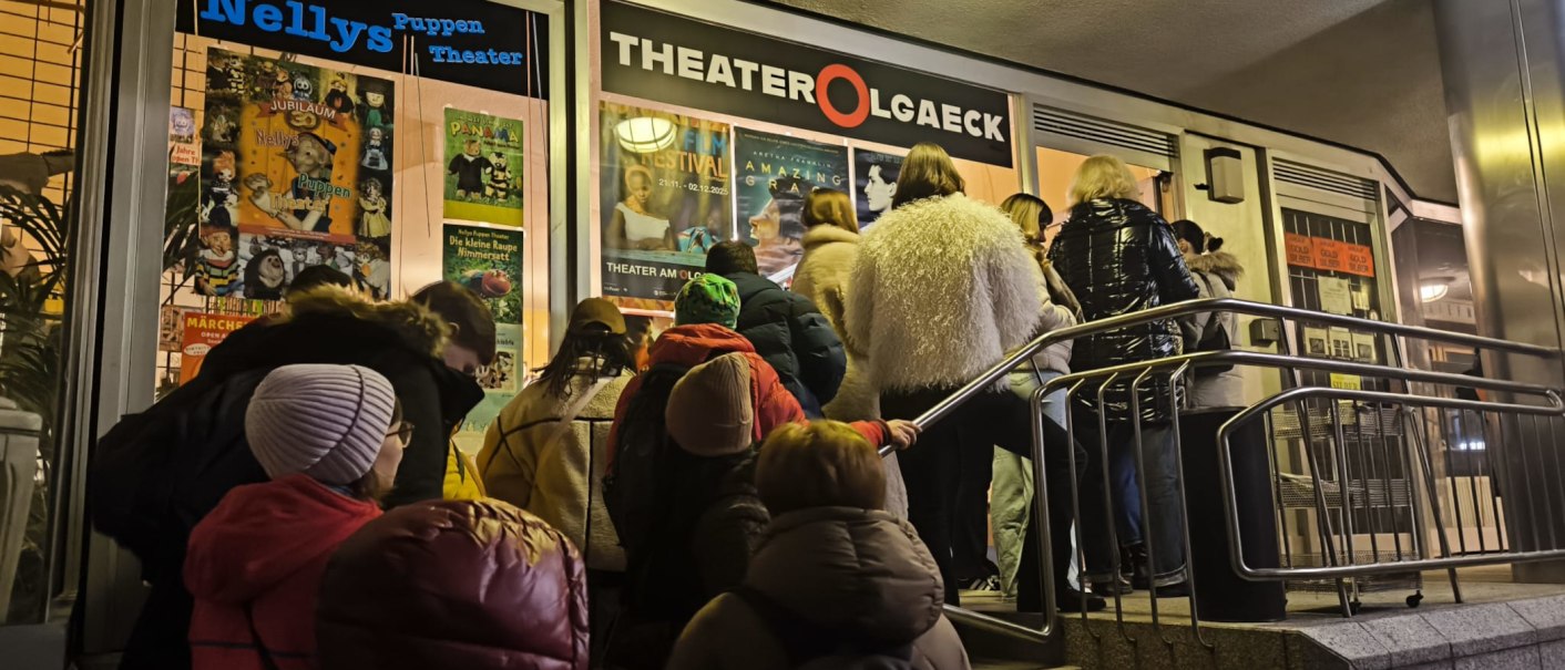 An evening line outside the Theater am Olgaeck in Stuttgart, with posters advertising a puppet show and a film festival., © Theater am Olgaeck An evening line outside the Theater am Olgaeck in Stuttgart, with posters advertising a puppet show and a film festival., © Theater am Olgaeck