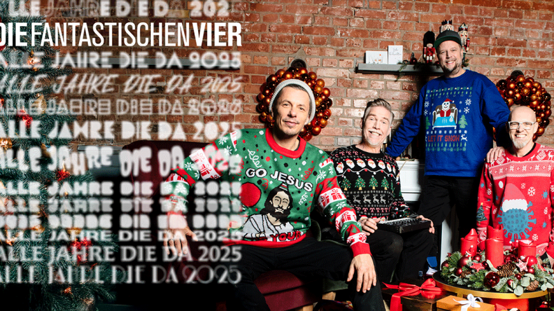 Vier M&auml;nner in bunten Weihnachtspullovern posieren vor einer festlich dekorierten Backsteinwand. Der Raum ist mit Weihnachtsdekoration geschm&uuml;ckt., &copy; links im Bild