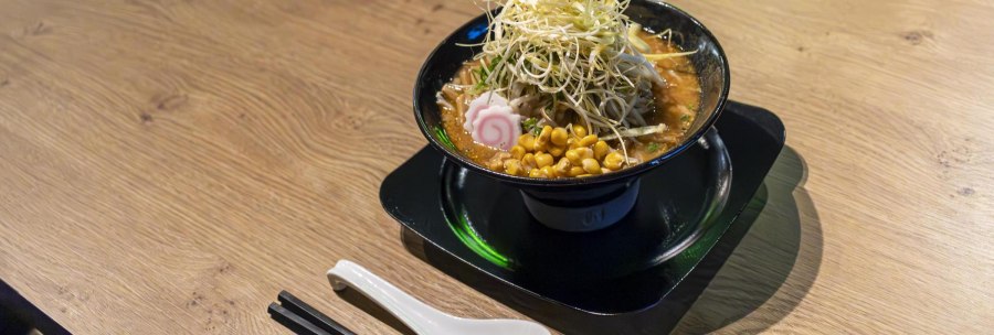 Eine Sch&uuml;ssel Ramen mit Mais, Narutomaki und Gem&uuml;se auf einem Holztisch. Daneben liegen Essst&auml;bchen und ein L&ouml;ffel., &copy; SMG, Sarah Schmid