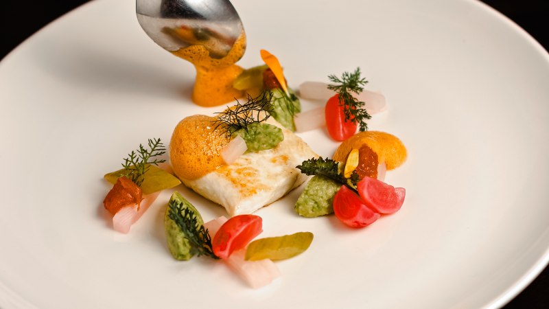 Heilbutt mit Avocado, Radieschen und Schaum kunstvoll auf weißem Teller angerichtet, mit Löffel serviert., © Hupperts
