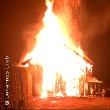 Ein Haus steht in Flammen und leuchtet hell in der Dunkelheit. Die Flammen schlagen hoch aus dem Dach., © links im Bild Ein Haus steht in Flammen und leuchtet hell in der Dunkelheit. Die Flammen schlagen hoch aus dem Dach., © links im Bild