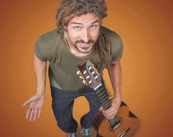 Ein Mann mit Dreadlocks h&auml;lt eine Gitarre und hat einen kleinen Vogel auf dem Kopf. Er tr&auml;gt ein gr&uuml;nes T-Shirt und steht vor einem orangefarbenen Hintergrund., &copy; Rosenau Kultur e.V.