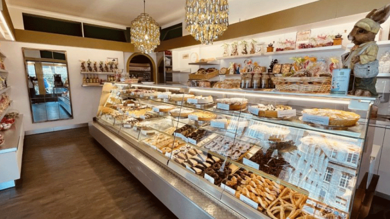 Ein gem&uuml;tliches Caf&eacute; mit einer Vitrine voller Geb&auml;ck und Schokolade. Dekorative Figuren und ein Kronleuchter erg&auml;nzen das Ambiente., &copy; FreCla Gastronomiebetriebe GmbH