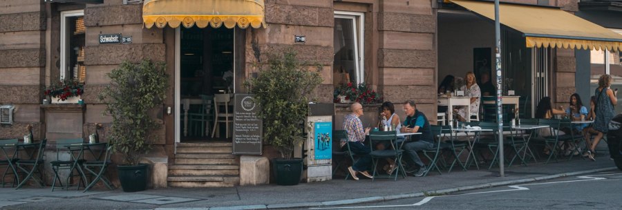 Caf&eacute; mit gelbem Vordach an einer Stra&szlig;enecke. G&auml;ste sitzen drau&szlig;en an Tischen. Schild mit 'Lumen' und Stra&szlig;enschild 'Schwabstr.' sichtbar., &copy; SMG, Sarah Schmid