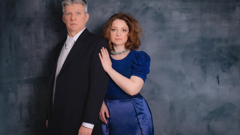Ein Mann im Anzug und eine Frau in einem blauen Kleid stehen vor einem grauen Hintergrund. Die Frau legt ihre Hand auf die Schulter des Mannes., © Diana Hajdu, Peter Cser Ein Mann im Anzug und eine Frau in einem blauen Kleid stehen vor einem grauen Hintergrund. Die Frau legt ihre Hand auf die Schulter des Mannes., © Diana Hajdu, Peter Cser