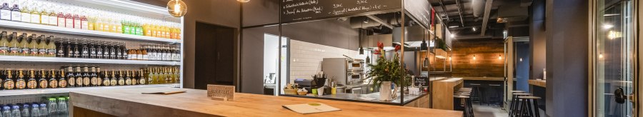 Modernes Café mit Holztischen, Getränkekühlschrank und hängenden Glühbirnen. An der Wand steht "Martha's". Gemütliche Atmosphäre mit Barbereich., © Martha's, Stuttgart