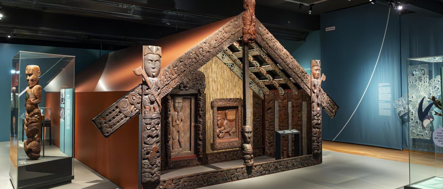 Exhibition in the Linden-Museum Stuttgart with an artistically carved Maori house and figures. The exhibits are richly decorated and detailed., © SMG Stuttgart Marketing GmbH - Sarah Schmid