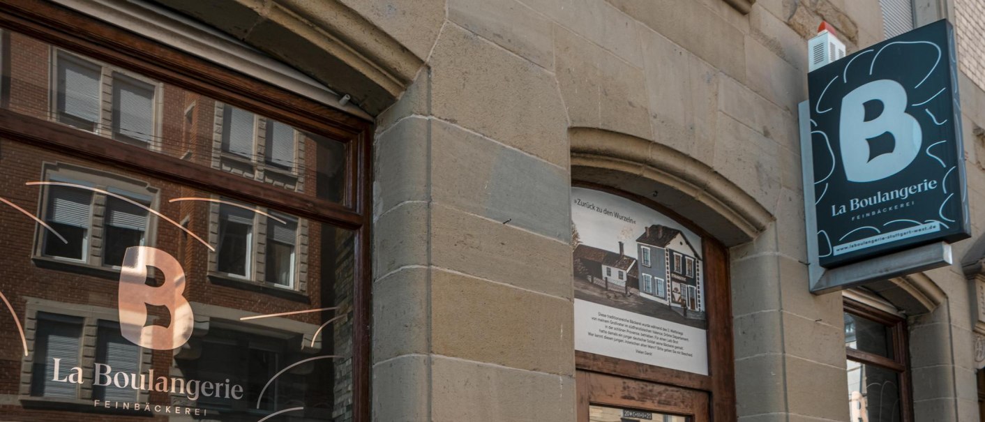 Außenansicht der Bäckerei 'La Boulangerie' mit Schaufenster und Schild. Das Gebäude hat eine steinerne Fassade und spiegelt umliegende Architektur wider., © SMG, Sarah Schmid