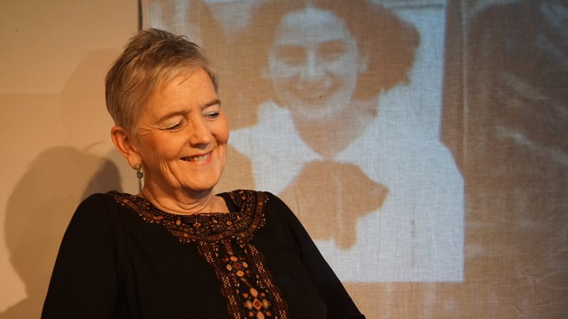 Eine Frau l&auml;chelt, w&auml;hrend im Hintergrund ein Schwarz-Wei&szlig;-Foto einer anderen Frau projiziert wird. Die Szene wirkt nostalgisch und warm., &copy; Katja Ritter