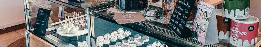 A display case in a caf&eacute; shows a selection of cupcakes, cake pops and pastries. Next to it are jars of cookies and price tags., &copy; Cupcakes & Bagels, Stuttgart