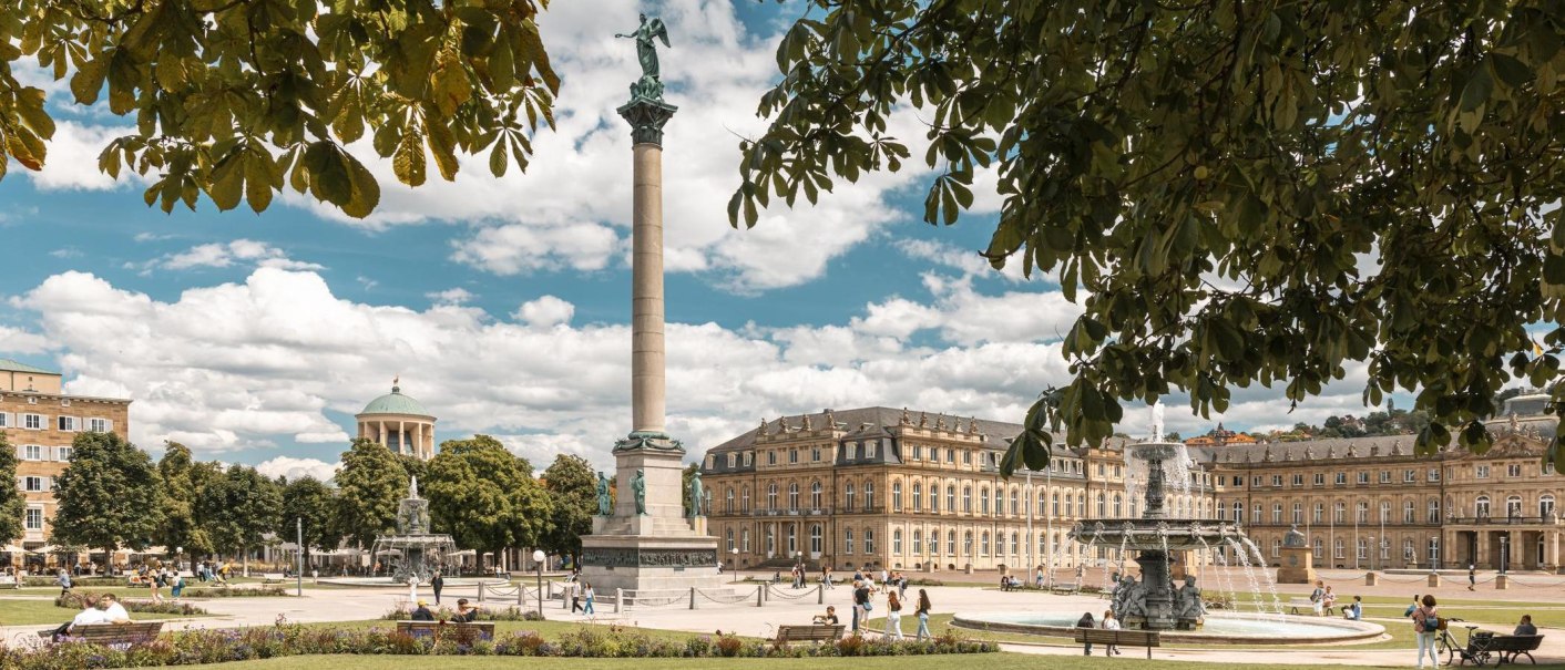 Der Schlossplatz in Stuttgart zeigt die Jubiläumssäule und das Neue Schloss. Menschen genießen den sonnigen Tag, während Bäume den Platz säumen., © SMG, Sarah Schmid Der Schlossplatz in Stuttgart zeigt die Jubiläumssäule und das Neue Schloss. Menschen genießen den sonnigen Tag, während Bäume den Platz säumen., © SMG, Sarah Schmid