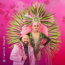 Two people in extravagant costumes in front of a pink background. One person is wearing an eye-catching feather costume., © see on the left Two people in extravagant costumes in front of a pink background. One person is wearing an eye-catching feather costume., © see on the left