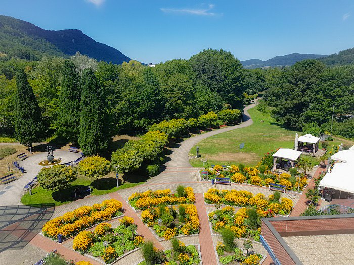 Blick aus einem Zimmer auf einen Park mit bunten Blumenbeeten, Bäumen und einem geschwungenen Weg. Im Hintergrund sind Hügel zu sehen., © ©hotel-graf-eberhard.de