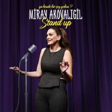 Eine Frau steht auf einer Bühne vor einem Mikrofon, trägt ein dunkles Outfit. Der Hintergrund ist ein lila Vorhang. Oben steht 'Miray Akovaligil Stand Up'., © links im Bild