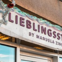 Lettering in red letters on a white background: "Lieblingsst&uuml;ck by Manuela Zinser", two large shop windows are located to the left and right of the entrance door., &copy; SMG Stuttgart Marketing GmbH - Sarah Schmid
