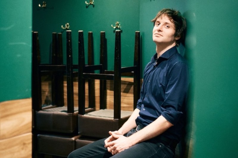A man with brown hair and a blue shirt smiles at the camera in front of a neutral background., &copy; Renitenztheater Stuttgart e.V.