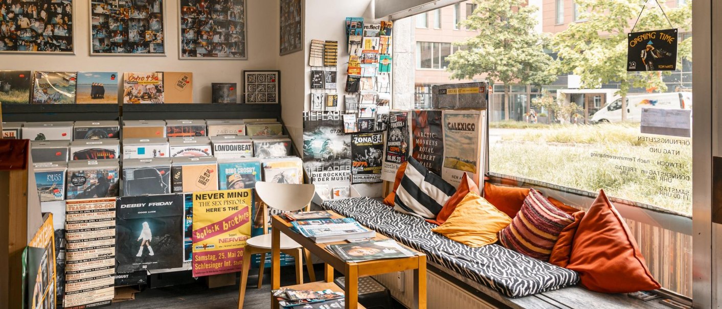 A record store with vinyls, posters and a cozy seating area with cushions. Large window front with a view to the outside., © SMG, Sarah Schmid