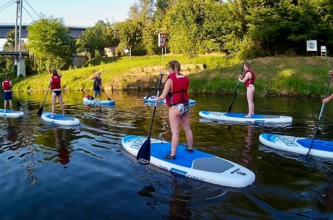 Eine Gruppe von Menschen in roten Schwimmwesten macht einen SUP-Anfängerkurs auf einem ruhigen Fluss, umgeben von grüner Natur., © Cool-Tours StattReisen